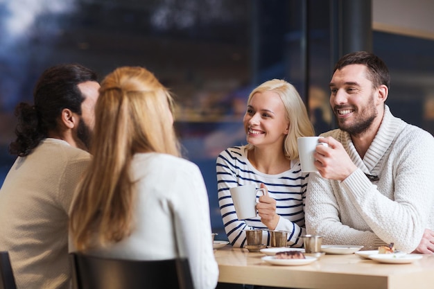 concetto di persone, tempo libero, comunicazione, mangiare e bere - amici felici che si incontrano e bevono tè o caffè al bar