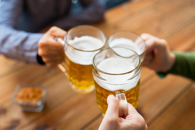 concetto di persone, tempo libero e bevande - primo piano di mani maschili che tintinnano boccali di birra al bar o al pub