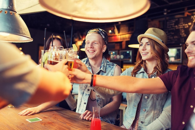 concetto di persone, tempo libero, feste e feste - gruppo di amici sorridenti felici che tintinnano bicchieri con bevande al bar o pub