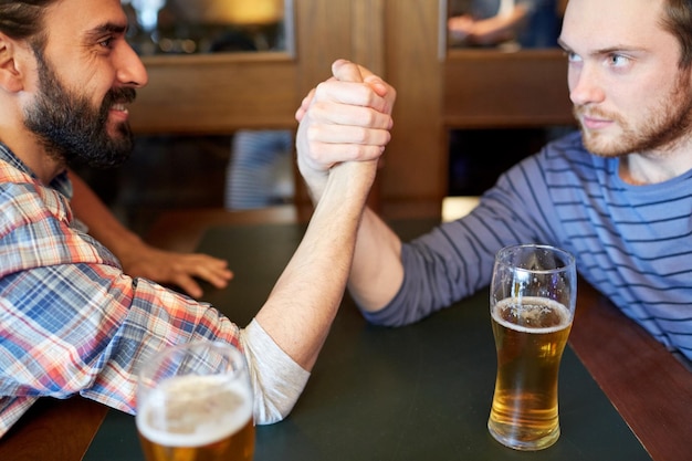 concetto di persone, tempo libero, sfida, competizione e rivalità - amici maschi felici che lottano con il braccio e bevono birra alla spina al bar o al pub