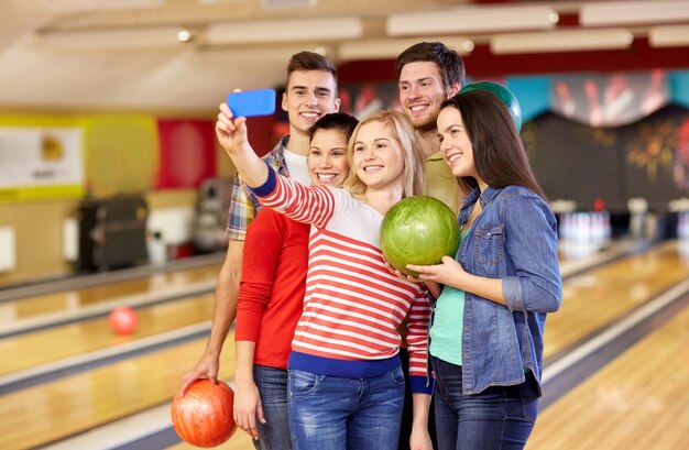 concetto di persone, tempo libero, sport, amicizia e intrattenimento - amici felici che prendono selfie con lo smartphone nel club di bowling