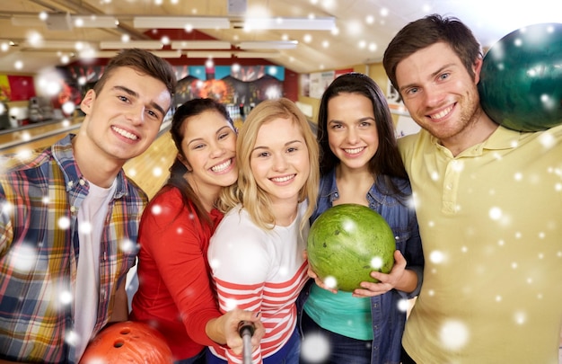 concetto di persone, tempo libero, sport, amicizia e intrattenimento - amici felici che si fanno selfie con lo smartphone sul monopiede nel club di bowling durante la stagione invernale