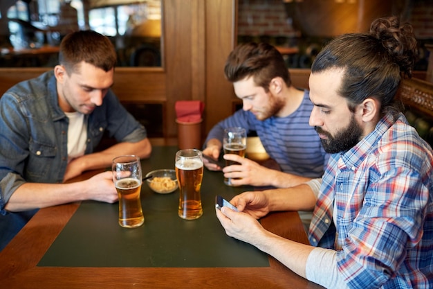 concetto di persone, uomini, tempo libero, amicizia e comunicazione - amici maschi con smartphone che bevono birra alla spina al bar o al pub