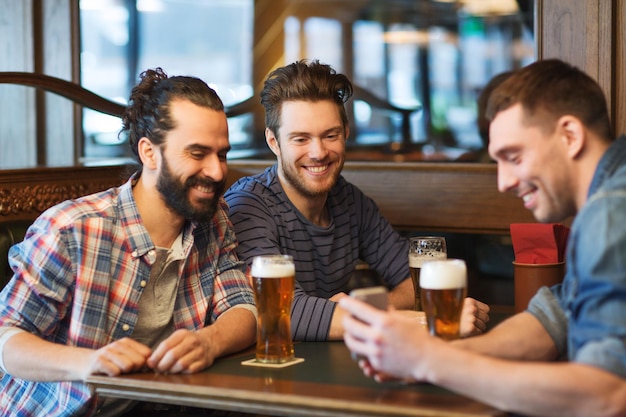 concetto di persone, uomini, tempo libero, amicizia e tecnologia - amici maschi felici con smartphone che bevono birra al bar o al pub