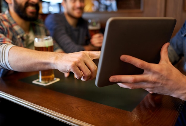 concetto di persone, uomini, tempo libero, amicizia e tecnologia - primo piano di amici maschi felici con computer tablet pc che bevono birra al bar o al pub