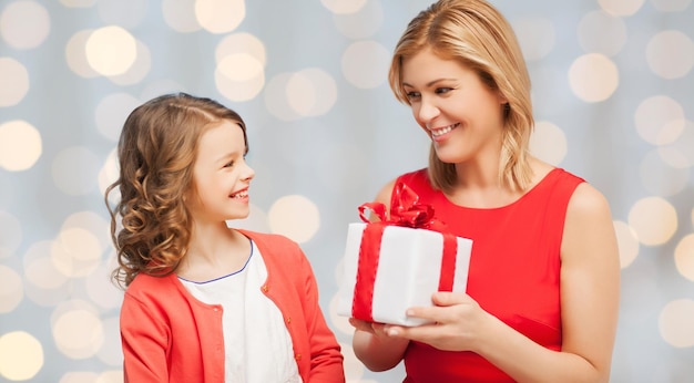 concetto di persone, vacanze, natale e famiglia - madre e figlia felici che danno e ricevono confezione regalo su sfondo di luci natalizie