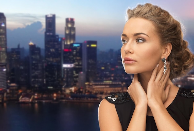 concetto di persone, vacanze, vita notturna e glamour - bella donna che indossa orecchini su sfondo serale della città di singapore