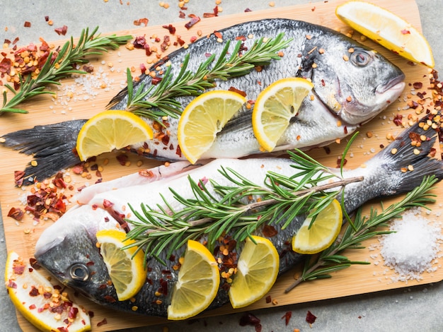 Concetto di pesce mediterraneo. Pesce crudo di dorado con limone, spezie e rosmarino su tavola di legno. Orata biologica fresca o pesce dorada. Vista dall'alto