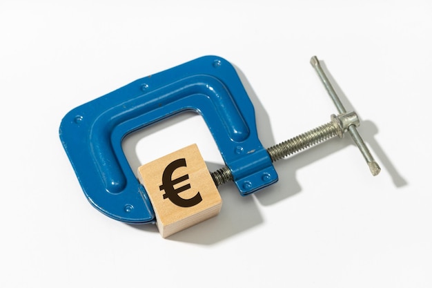 Concetto di politica di inasprimento monetario Il morsetto comprime il segno dell'euro sul blocco di legno