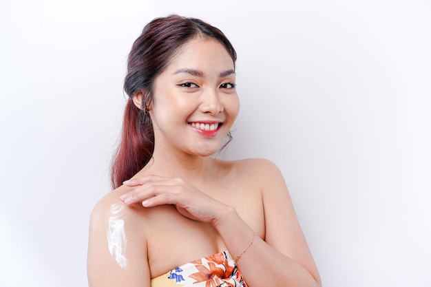 Concetto di prodotti per la cura della pelle Donna asiatica che applica una lozione idratante sul corpo dopo la doccia in piedi avvolta in un asciugamano ritagliato