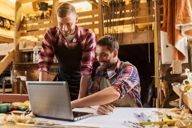 concetto di professione, falegnameria, tecnologia e persone - due falegnami con computer portatile e progetto in officina