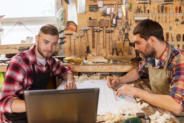 concetto di professione, falegnameria, tecnologia e persone - due falegnami con computer portatile e progetto in officina