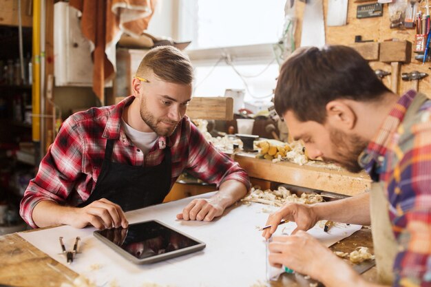 concetto di professione, tecnologia e persone - due operai con computer tablet pc e progetto in officina