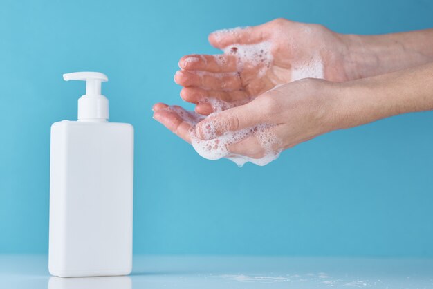 Concetto di protezione della salute dell'epidemia COVID-19 con antisettico. Mani di lavaggio della donna utilizzando disinfettante o gel antisettico come misura di prevenzione per coronavirus su sfondo blu