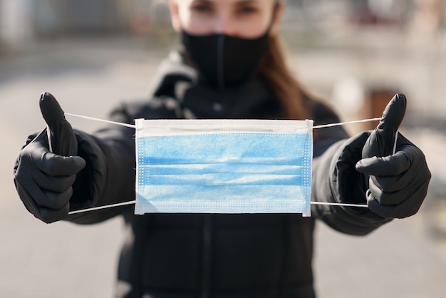 Concetto di protezione ed epidemia. Giovane ragazza asiatica adulta con tenuta coperta della bocca e del naso nella maschera di protezione di sicurezza delle mani