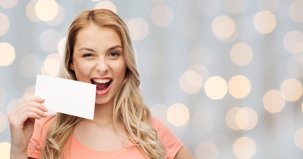 concetto di pubblicità, invito, messaggio e persone - giovane donna sorridente o adolescente con carta di carta bianca vuota su sfondo di luci di vacanza