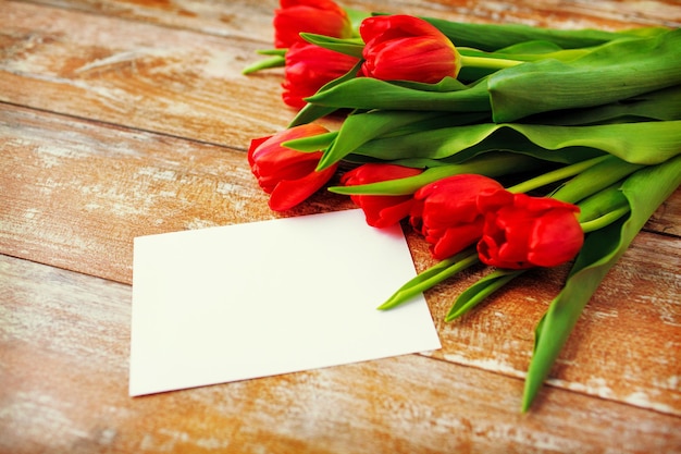 concetto di pubblicità, San Valentino, saluto e vacanze - primo piano di tulipani rossi e carta bianca o lettera su fondo di legno