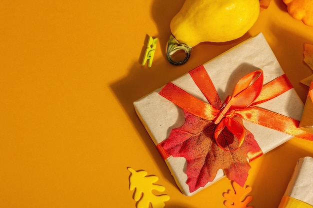 Concetto di regalo in colori autunnali. Scatole avvolte, decorazioni autunnali festive, zucca, foglie e bacche. Una luce dura alla moda, un'ombra scura, uno sfondo arancione, uno spazio di copia