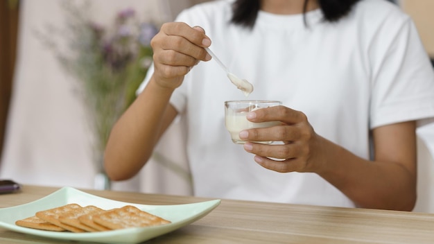 Concetto di relax domestico Giovane donna che mangia yogurt e cracker per uno spuntino mentre si rilassa a casa