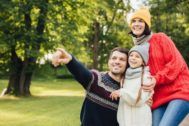 Concetto di relazione per la stagione familiare La famiglia amichevole e affettuosa ha una passeggiata nel parco autunnale ammira la bellissima natura indossa vestiti caldi a maglia puntati in lontananza come mostra qualcosa di interessante