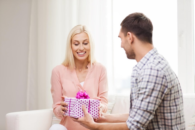 concetto di relazioni, amore, persone, compleanno e vacanze - uomo felice che dà una confezione regalo donna a casa