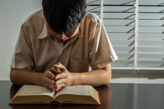 Concetto di religione Giovane uomo asiatico che legge la Bibbia e alza le mani alla preghiera per credere nella bontà