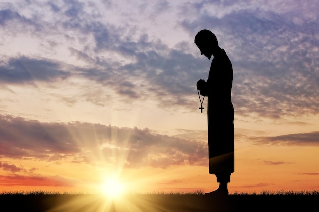 Concetto di religione. Sagoma di un prete con una croce in mano contro il tramonto