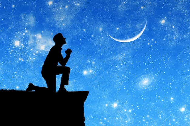 Concetto di religione. Siluetta dell'uomo che prega sullo sfondo del cielo con la luna e le stelle