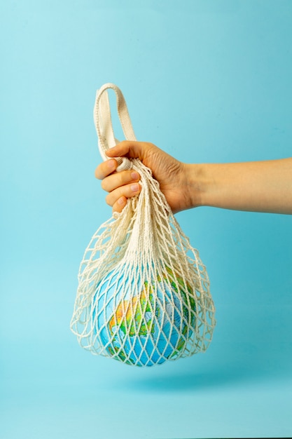 Concetto di rifiuti zero. Borsa a tracolla in una mano femmina con globo terrestre. Sacchetti di plastica gratuiti