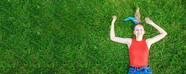 Concetto di rilassamento e meditazione. La giovane ragazza bionda si trova sull'erba verde esamina la macchina fotografica fuori nel parco.