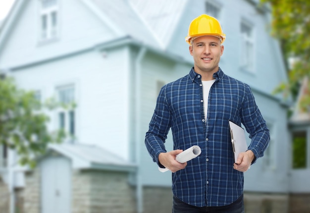 concetto di riparazione, costruzione, costruzione, persone e manutenzione - costruttore maschio sorridente o lavoratore manuale in casco con progetto e appunti su sfondo di casa vivente