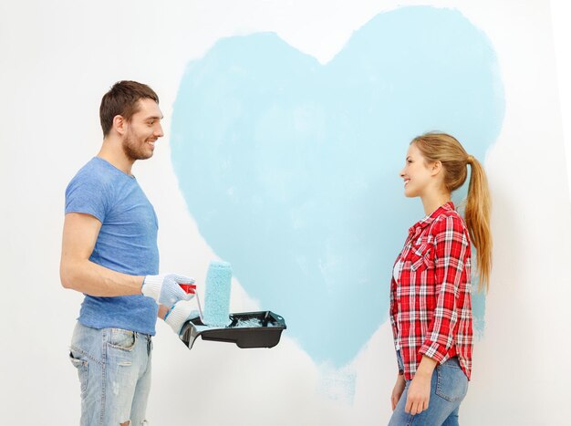 concetto di riparazione, costruzione e casa - coppia sorridente che dipinge un grande cuore sul muro di casa