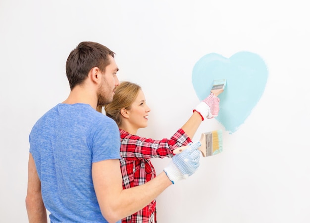 concetto di riparazione, costruzione e casa - coppia sorridente che dipinge un piccolo cuore sul muro di casa