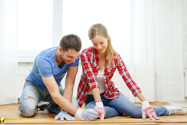 concetto di riparazione, costruzione e casa - coppia sorridente che misura il pavimento in legno