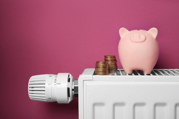 Concetto di risparmio Piggy bank e denaro per il radiatore di riscaldamento con regolatore di temperatura su sfondo rosa