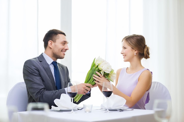 concetto di ristorante, coppia e vacanza - uomo sorridente che dà alla fidanzata o alla moglie un mazzo di fiori al ristorante