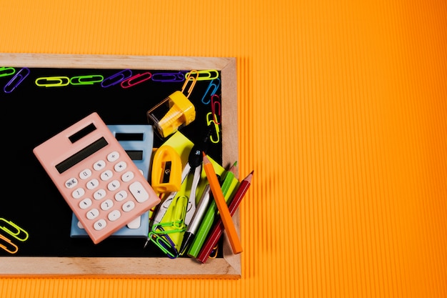 Concetto di ritorno a scuola. Attrezzatura di istruzione sulla lavagna su fondo arancio.