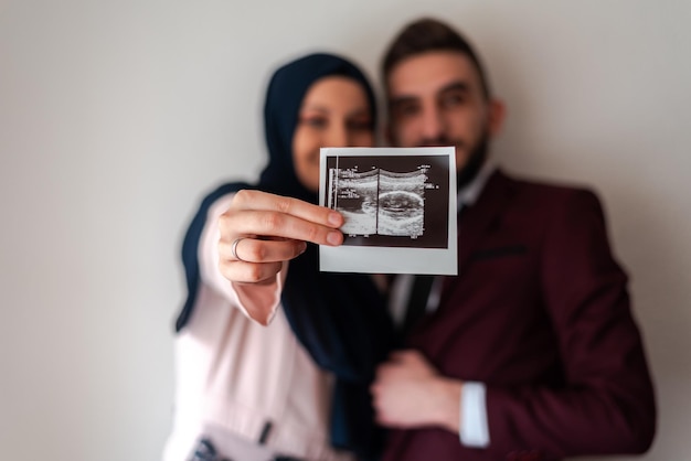 Concetto di rivelazione di genere Felice coppia musulmana incinta che tiene la foto ecografica del bambino