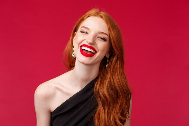 Concetto di romanticismo, eleganza, bellezza e donne. Ritratto di Close-up di felice, allegra donna rossa in lussuoso abito nero, rossetto rosso, godendo la festa o la data, ridendo sorriso raggiante