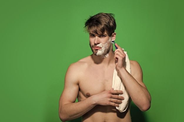 Concetto di routine mattutina uomo radersi il viso barbuto su sfondo verde scapolo con rasoio per crema da barba