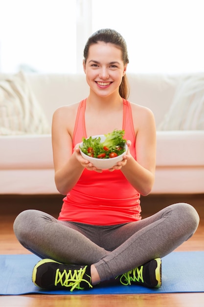 concetto di salute, dieta, casa e felicità - sorridente ragazza sportiva con insalata verde a casa