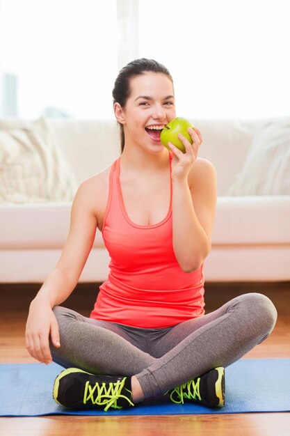 concetto di salute, dieta, casa e felicità - sorridente ragazza sportiva con mela verde a casa