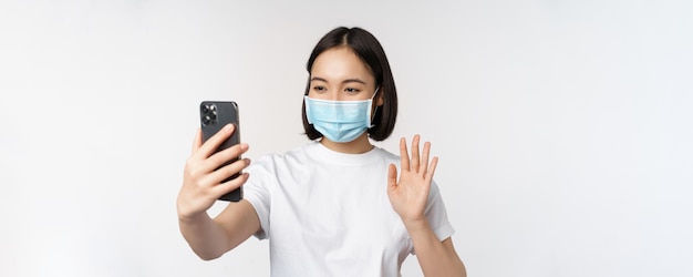 Concetto di salute e covid Studentessa asiatica moderna in video chat con maschera medica con telefono cellulare wavi