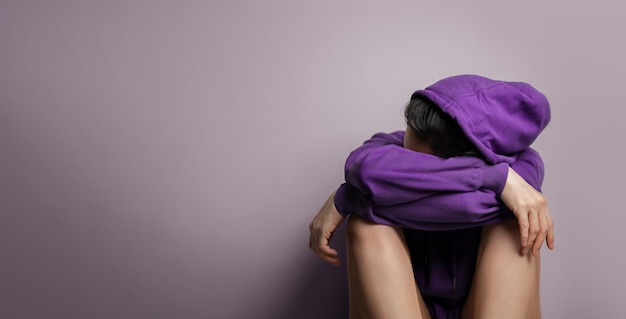 Concetto di salute mentale una felpa con cappuccio da ansia da stress e depressione Donne sedute vicino al muro più spazio per le copie sulla sinistra Tono blu viola