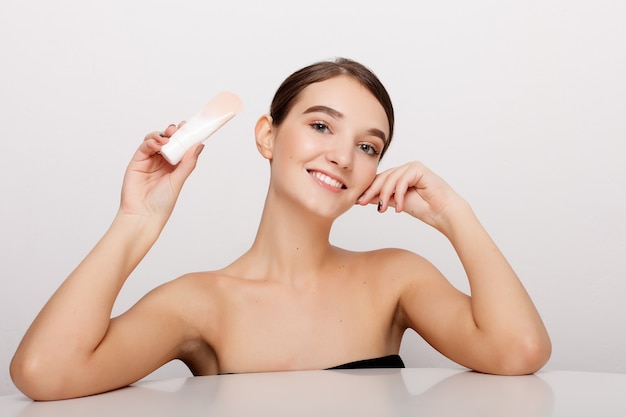 Concetto di salute, persone e bellezza - volto di bellezza di giovane donna con crema cosmetica su una guancia. Concetto di cura della pelle. Ritratto del primo piano isolato su bianco. volto di giovane donna adulta con pelle fresca e pulita.