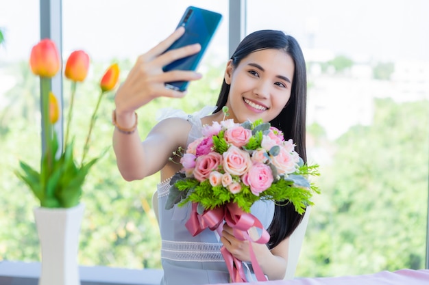 Concetto di San Valentino, selfie di felice di giovane femmina asiatica sorridente che si siede ad un alimento della tavola che tiene un mazzo delle rose nel ristorante