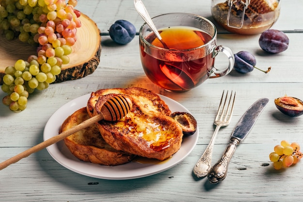 Concetto di sana colazione. Toast francesi con miele, frutta e tè sulla tavola di legno bianca