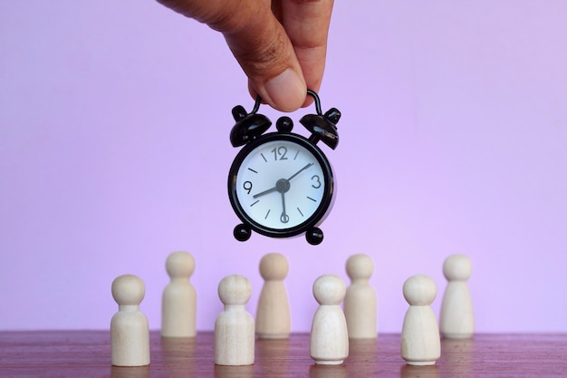 Concetto di scadenza del salario orario dell'orario di lavoro Sveglia e bambole di legno su sfondo viola