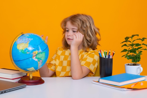 Concetto di scuola e istruzione Ritratto di un ragazzo carino che guarda il globo durante la lezione di geografia isolato su sfondo giallo studio Ritorno a scuola