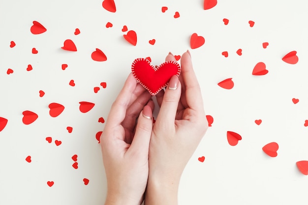 Concetto di sentimenti romantici. Vista superiore delle mani della signora che tengono il cuore rosso del feltro fatto a mano sul modello di amore bianco